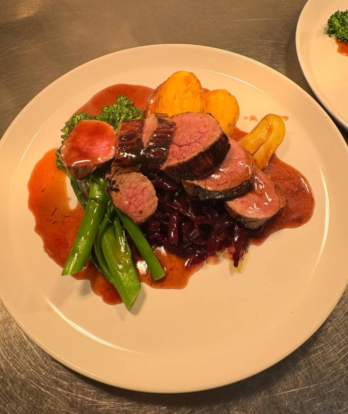 Rack of lamb sliced over roast potatoes and greens, in a red-wine jus -- a plate from the kitchen.