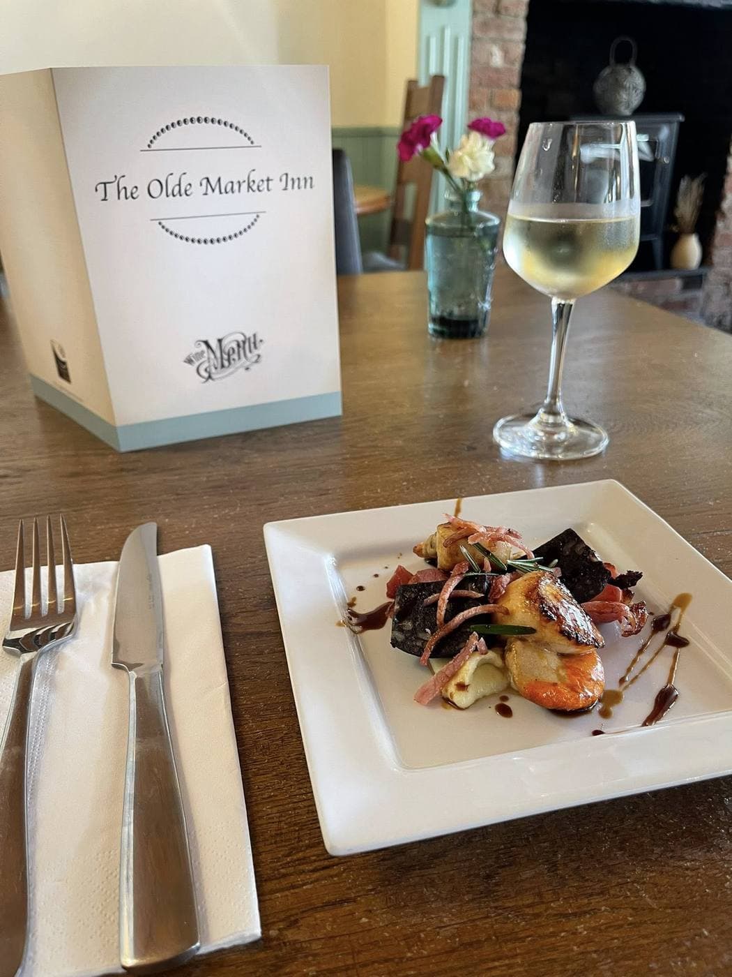 An Olde Market Inn menu stand on the table alongside a plate and a glass of white wine.