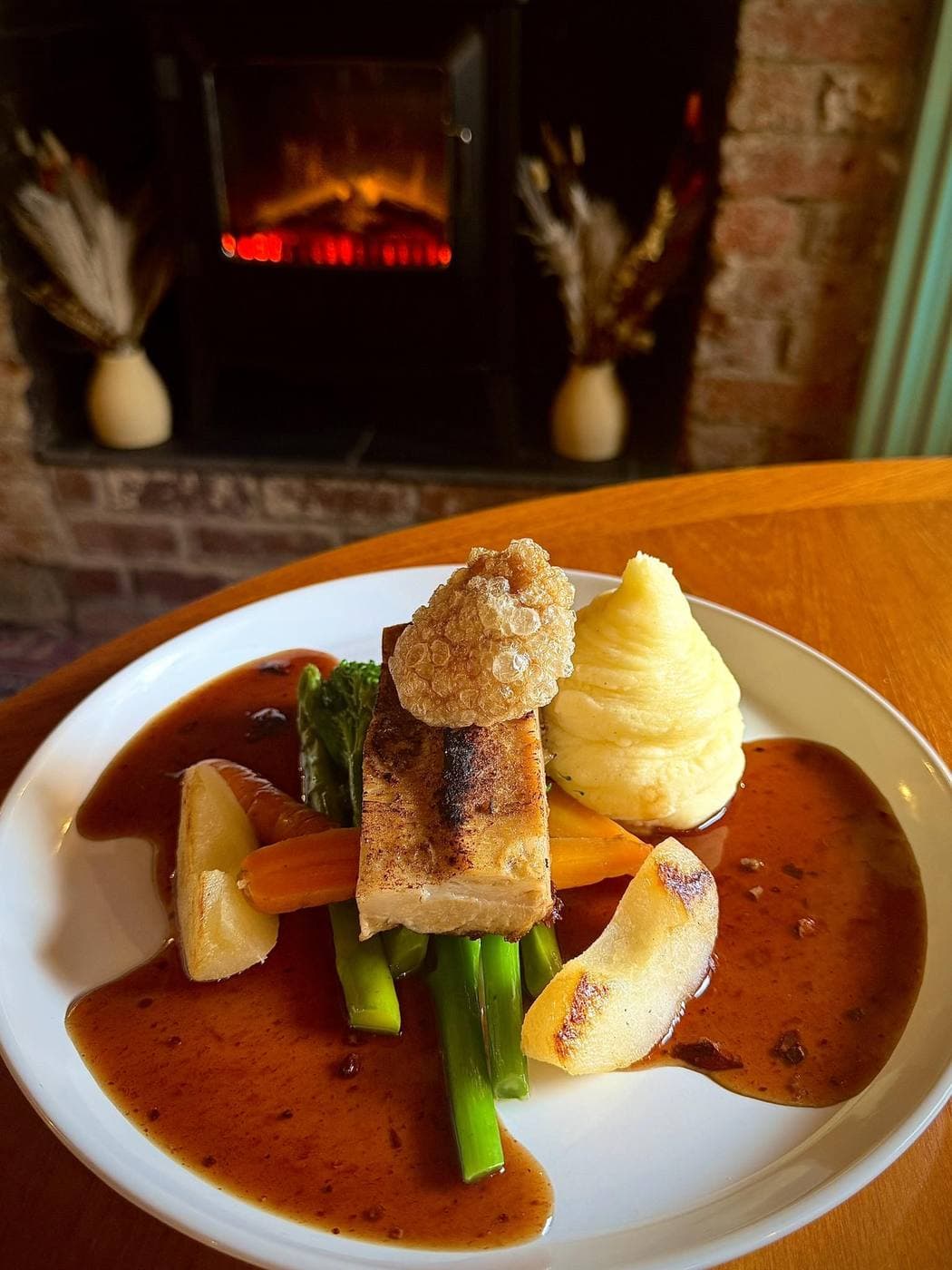 Pork belly with mashed potato, carrots, broccoli and crackling, served with a rich gravy -- wood-burner behind.