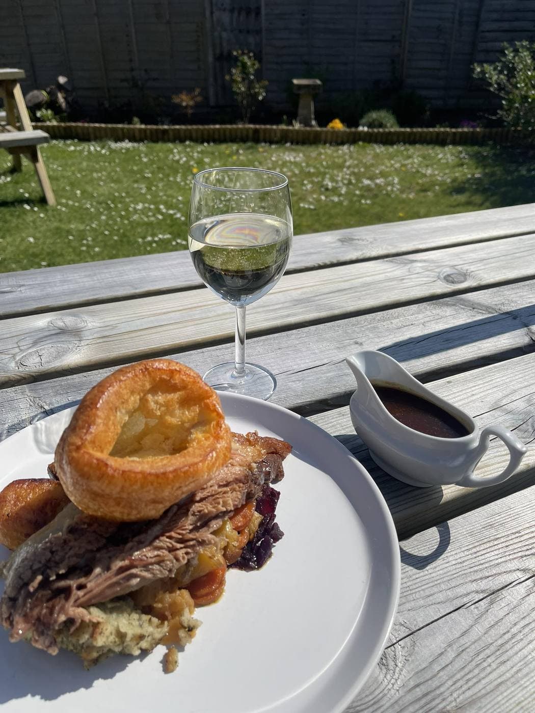 A Sunday roast plate in the beer garden -- Yorkshire pudding, sliced beef, red cabbage, with a jug of gravy and a glass of wine on the picnic table.