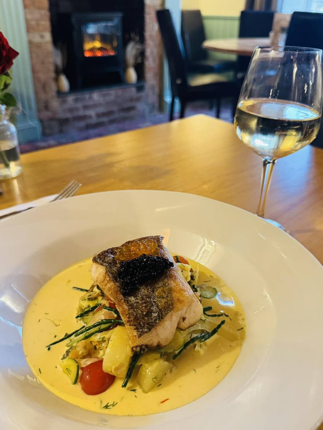 A plate of salmon in the restaurant -- wine glass and wood-burner in the background.